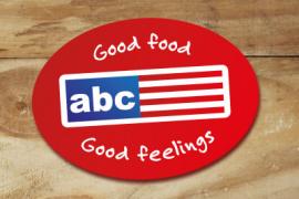 Rood ovalen ABC Restaurants-logo met tekst 'Good food Good feelings' op houten achtergrond.
