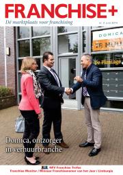 Twee mannen schudden handen buiten een gebouw, waarbij een van hen een sleutel overhandigt; vrouw staat ernaast.