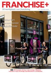 Twee medewerkers fietsen met bakfietsen voor een Bakker Bart filiaal, omringd door een boog van roze ballonnen.