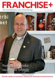 Een man in een net pak met een koffie in zijn hand voor een plank met koffieverpakkingen.