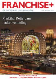 De Markthal in Rotterdam verlicht in de avond, omgeven door stadslichten en een kerktoren op de achtergrond.