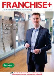 Man in pak met bril in een Specsavers-winkel, met op de achtergrond optische producten en een poster met tekst.