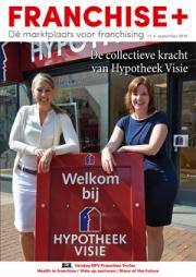 Twee vrouwen poseren buiten bij een Hypotheek Visie-vestiging met een welkomstbord op de voorgrond.