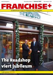 Twee mannen schudden elkaar de hand voor de ingang van The Read Shop, geflankeerd door groene slingers.
