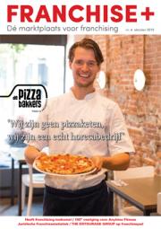 Man in pizzabakkersuniform presenteert een pizza met lach in horecaruimte voor Franchise+ editie oktober 2019.