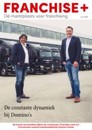 Twee mannen poseren voor een rij Domino's vrachtwagens bij een magazijn, in een uitgave van FRANCHISE+ juli 2020.
