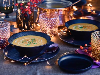 Feestelijk gedekte tafel met soepkommen, glazen en sfeerverlichting in kerstsfeer.
