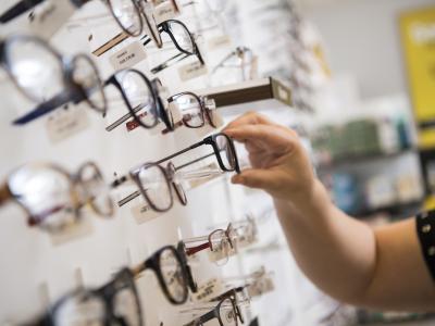 Hand kiest bril uit rek met diverse monturen in optiekwinkel.
