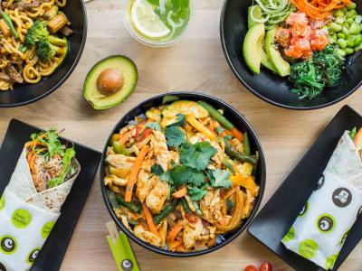 Diverse kleurrijke Aziatische gerechten van Eazie gepresenteerd op een houten tafel met wraps, bowls en een drankje.