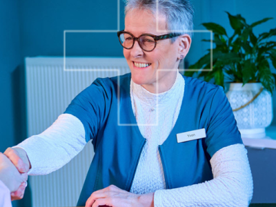 Medewerker schudt handen met klant aan bureau met computerscherm dat gezondheidsgegevens weergeeft in moderne kantoorruimte.