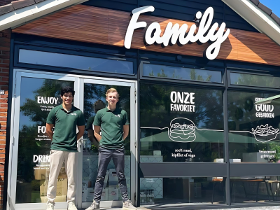 Twee personen in groene polo's staan voor de ingang van een nieuwe Family-vestiging in Markelo.