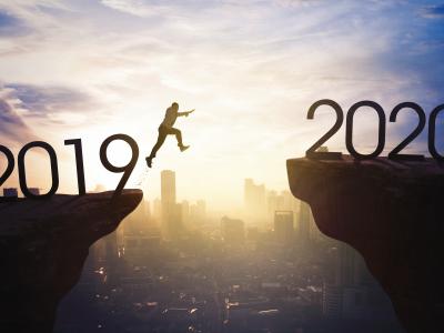 Persoon springt van een rots met 2019 naar een rots met 2020 boven een stadsgezicht bij zonsopgang.