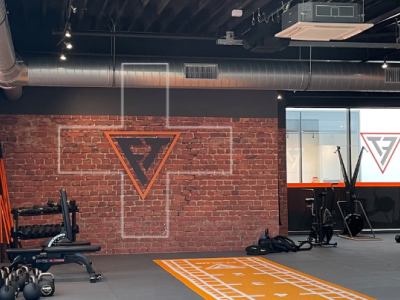 Fitnessstudio met diverse trainingsapparaten, inclusief gewichten, TRX-banden en sporttoestellen tegen een bakstenen muur.