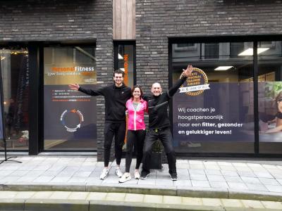 Drie mensen staan voor Personal Fitness Nederland studio naast een promotievlag en raamstickers over coaching.