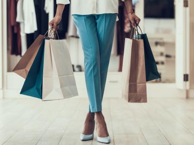 Persoon in winkel met meerdere papieren boodschappentassen, gekleed in blauwe broek en hakken.