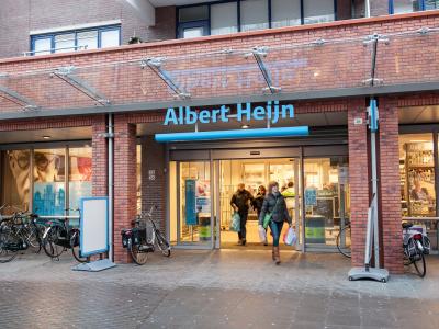 Vooraanzicht van een Albert Heijn winkel met klanten en geparkeerde fietsen aan de voorzijde.