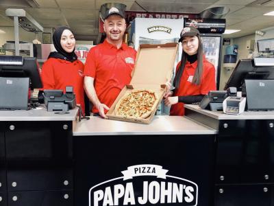 Drie medewerkers in rode uniformen presenteren een pizza in een Papa John’s Alexandrium vestiging.
