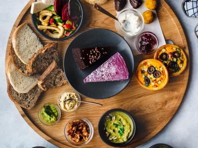 Diverse selectie van brunchgerechten met brood, taart, dips en quiches op een houten plank in een uitnodigende setting.