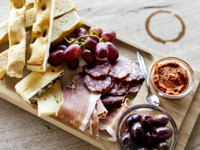 Een houten plank met stokbrood, kaas, druiven, vleeswaren, olijven en tapenade.