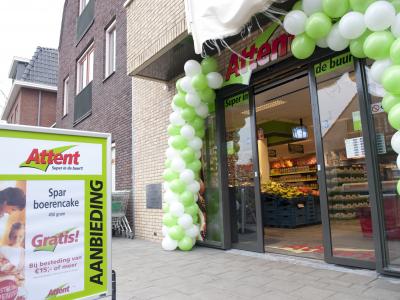 Entree van een Attent-supermarkt met groen-witte ballonnen en een bord met aanbiedingen.