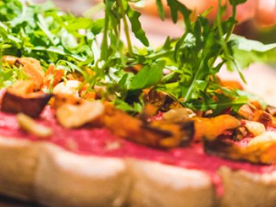 Vegetarische pizza met rode saus, rucola en geroosterde groenten op een houten tafel.