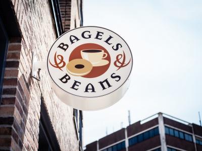 Rond uithangbord met het Bagels & Beans-logo aan een bakstenen gevel.