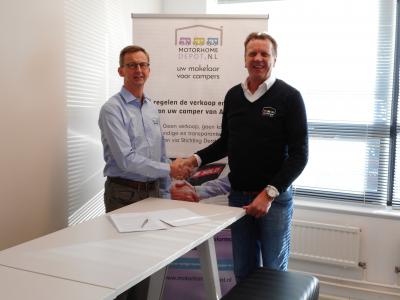 Twee mannen schudden handen voor een Motorhome Depot-bord bij het ondertekenen van een franchisedeal.