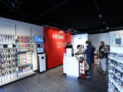 Interieur van een HEMA-winkel met klanten bij de kassa en rekken vol producten.