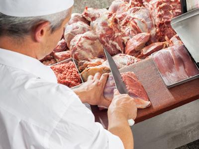 Slager snijdt vlees op een houten werkblad naast een weegschaal en verschillende stukken rauw vlees.