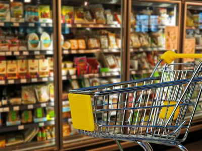 Winkelwagentje in een supermarktgang met gevulde koelvakken op de achtergrond.