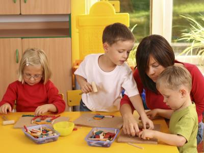 Kinderen en een volwassene bezig met educatief speelgoed aan een tafel in een kleurrijke kinderomgeving.