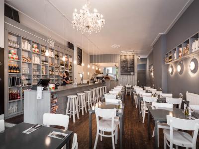 Interieur van een moderne pizzeria met witte stoelen, houten tafels en een lange bar met hoge krukken.