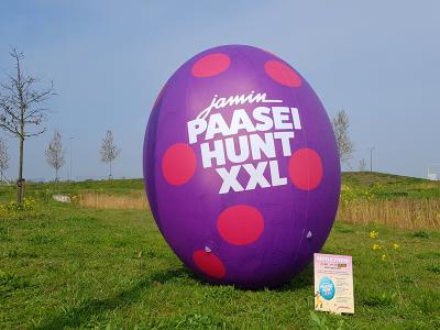 Opblaasbaar paasei met Jamin Paasei Hunt XXL logo staat in een groen landschap.