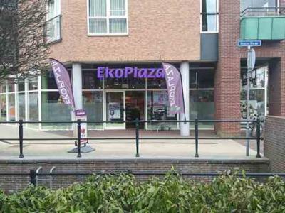Ekoplaza-winkelpand met paarse vlaggen voor de ingang in een stedelijke omgeving.