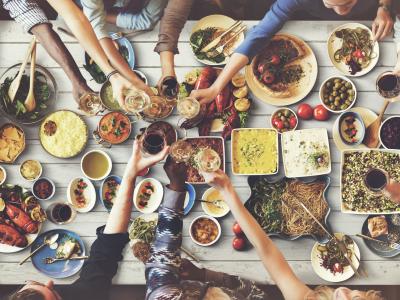 Bovenaanzicht van mensen die toosten en genieten van diverse gerechten aan een volle tafel in een gezellige setting.
