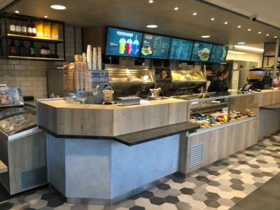 Interieur van een moderne Foodmaster met toonbank, menu's op schermen en een medewerker achter de balie.