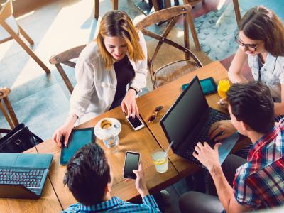 Een groep jonge professionals werkt samen aan een tafel met laptops, tablets en smartphones in een kantooromgeving.
