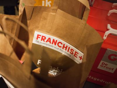 Bruine papieren tassen met Franchise+ tijdschrift en promotiemateriaal van een grafisch bedrijf.