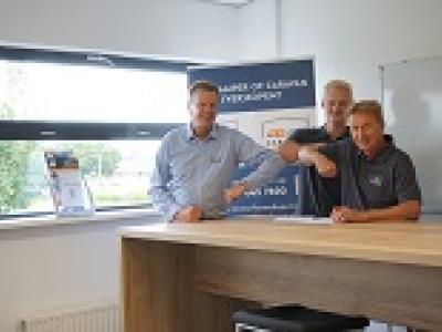 Drie mannen staan lachend bij een tafel in een kantoor met een promotiestand van Motorhome en Caravan Depot.