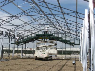 Constructiewerkers plaatsen metalen dakspanten op een bouwlocatie met behulp van een hoogwerker.