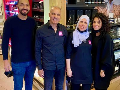 Vier mensen poseren glimlachend in een DA winkel met cosmetica producten op de achtergrond.