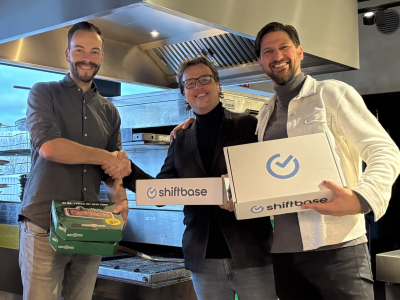 Drie mensen in een professionele keuken met New York Pizza en Shiftbase-dozen terwijl ze handen schudden.