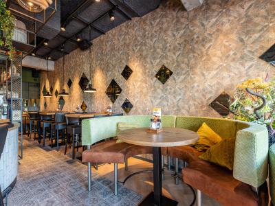 Interieur van De Beren restaurant met groene en bruine zitplekken, planten, en geometrische muurdecoraties.