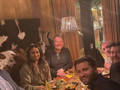 Zes mensen zitten samen aan een eettafel met borden en glazen in een gezellige setting.