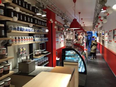 Interieur van een ijswinkel met volle schappen, rode accenten en klanten die bij de toonbank wachten.