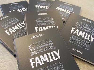 Stapels jubileumboeken met Family op de cover, uitgegeven door FHC Formulebeheer, liggen op een tafel.