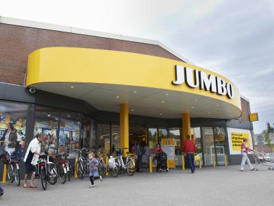 Voorzijde van een Jumbo-supermarkt met klanten die naar binnen gaan en fietsen geparkeerd voor de ingang.