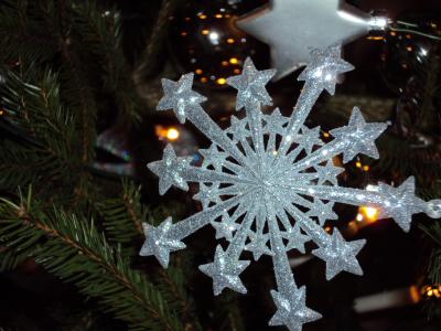 Glitterende sneeuwvlok-kerstdecoratie met sterren hangt in een met lichtjes versierde kerstboom.
