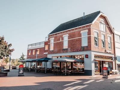 Rood bakstenen gebouw met Kwalitaria Délifrance in Winschoten, voorzien van terras met tafels en parasols.