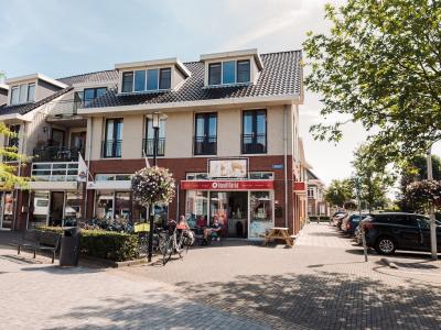 Kwalitaria De Batehof op een zonnige dag met klanten op het terras en fietsen voor de deur in een gezellige winkelstraat.